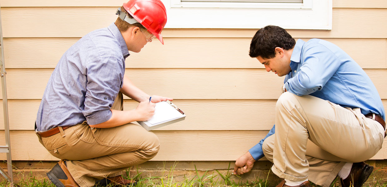 Two men inspecting the outside foundation of a house