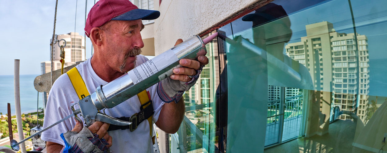 Worker caulking a window on upper floors of condo