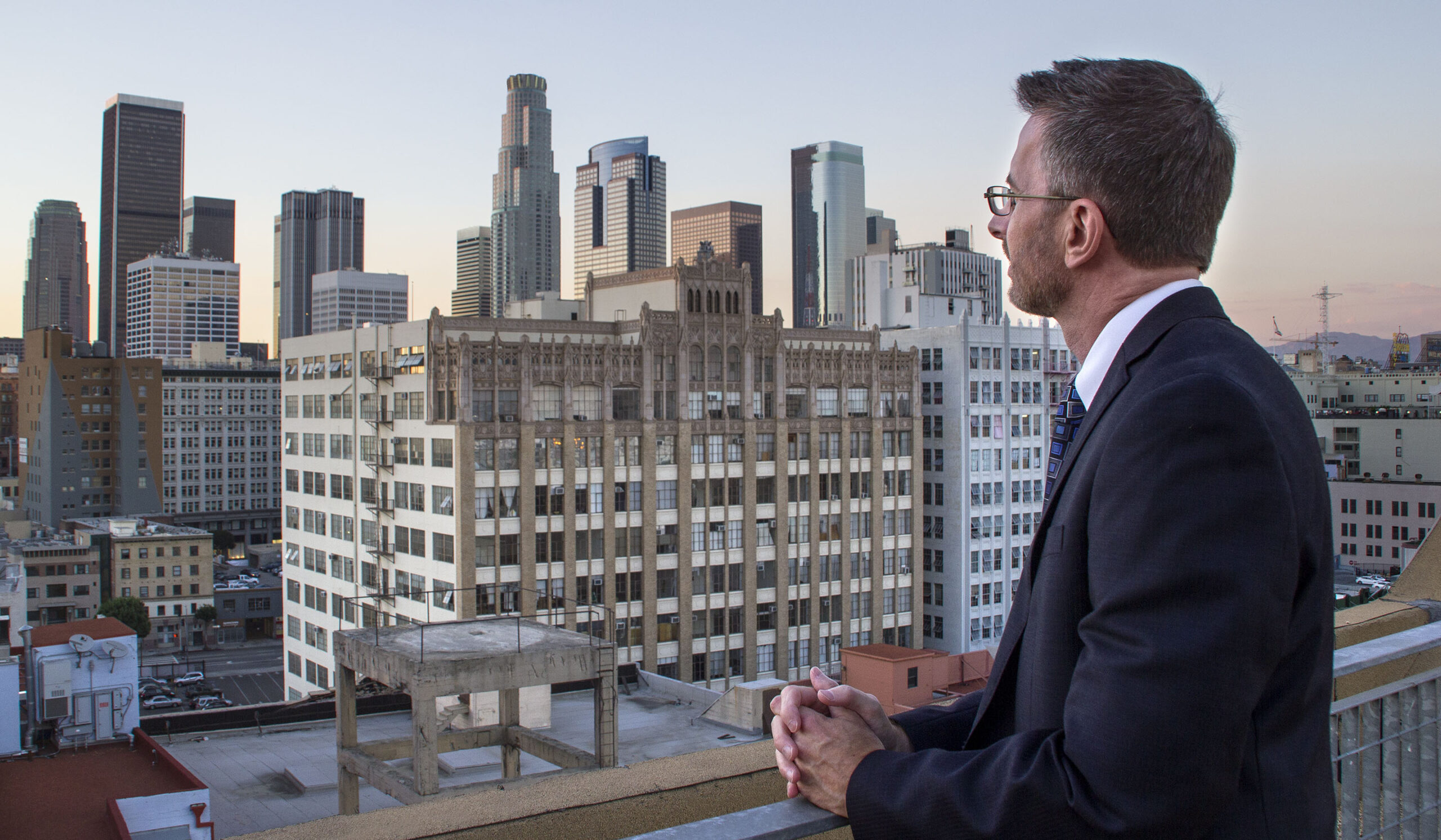 Condominium manager looking at the city skyline. The man is dressed in a suit. The view is during blue hour after sunset at the historic core of the city.