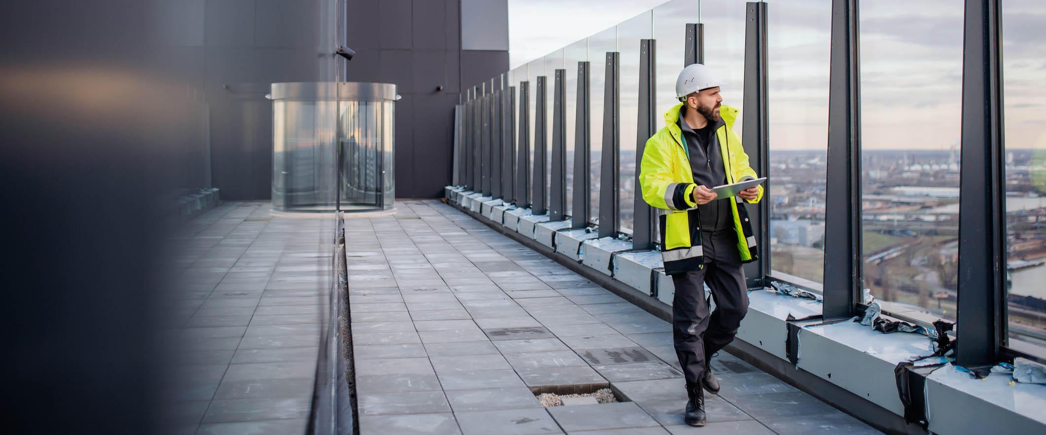 Mature man engineer walking on construction site, holding tablet with blueprints.