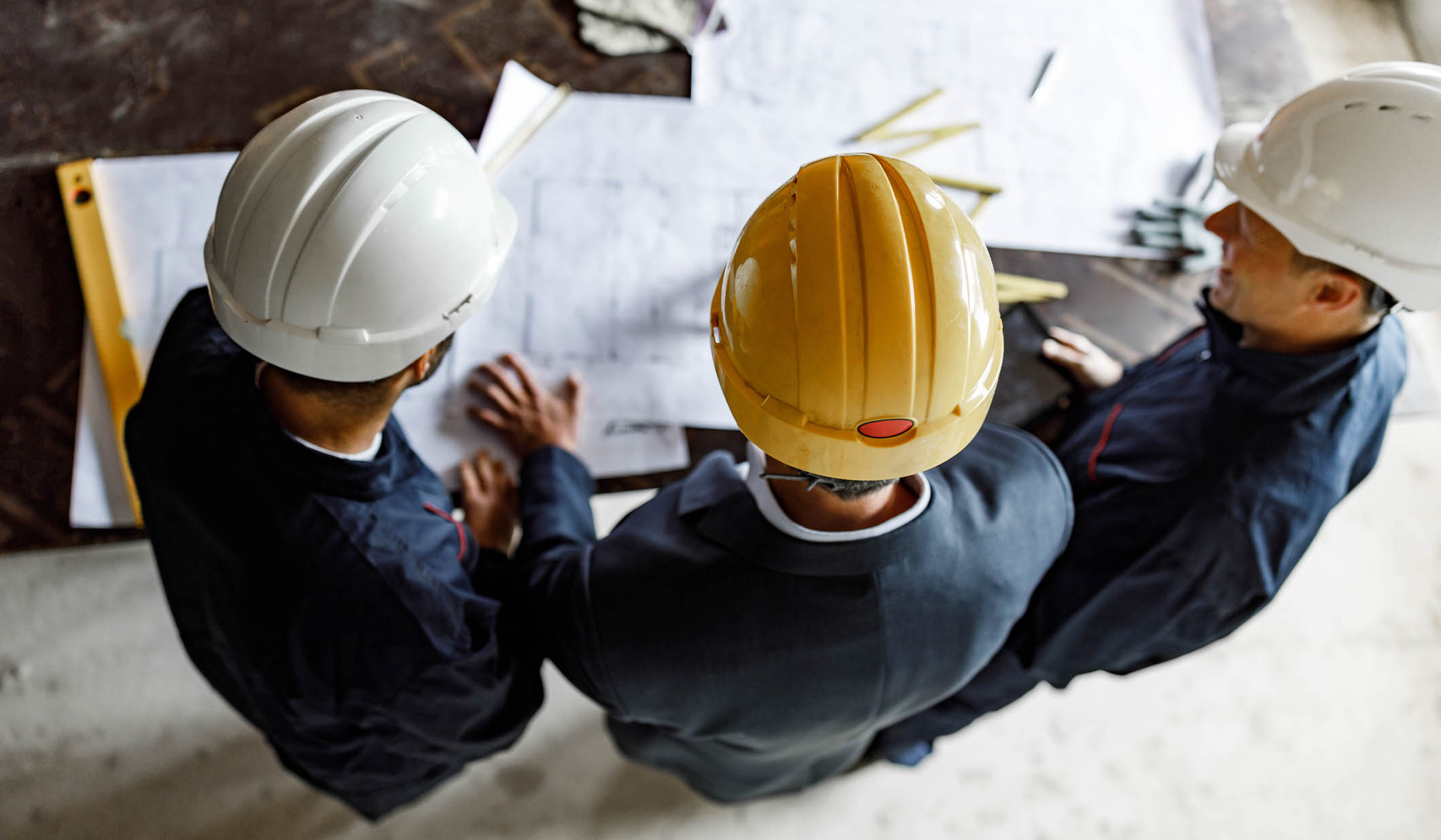 High angle view of manual workers and their foreman analyzing blueprints at construction site.