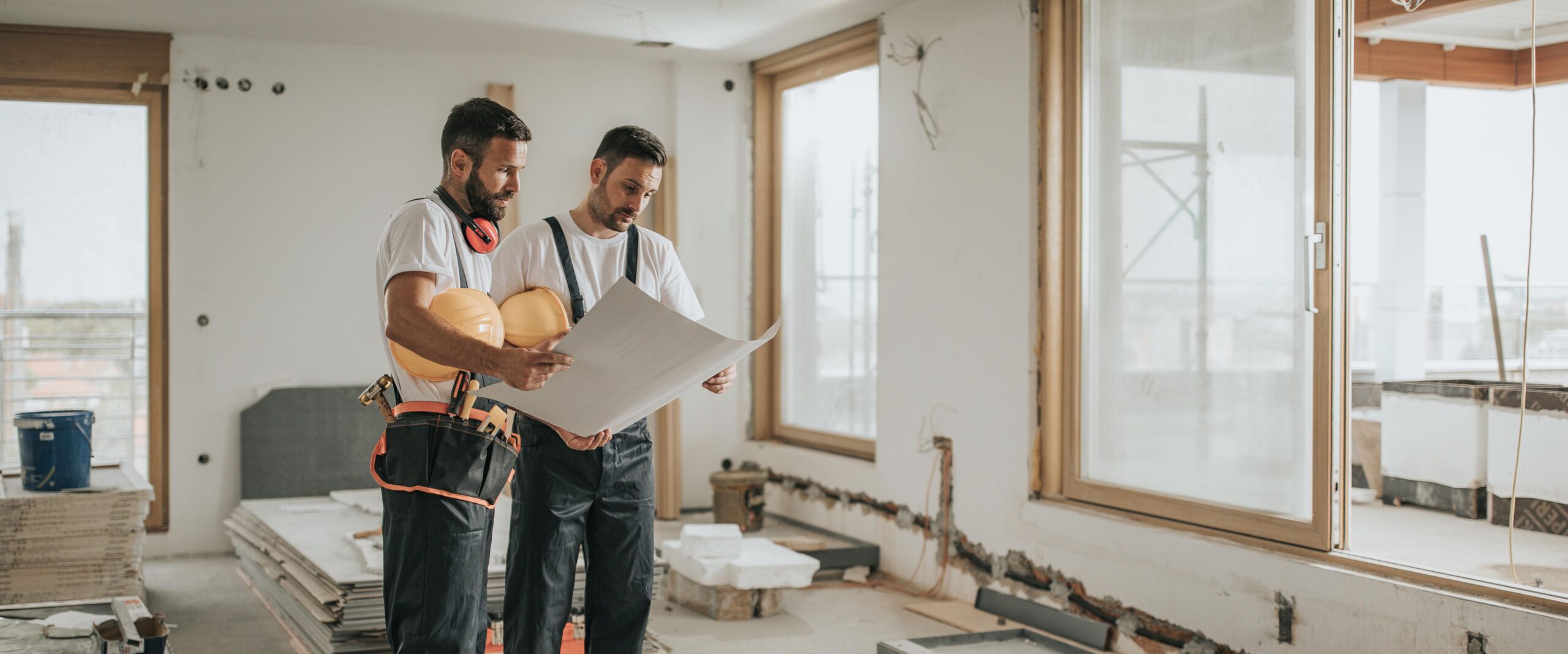 Young manual workers standing at construction site and examining blueprints.