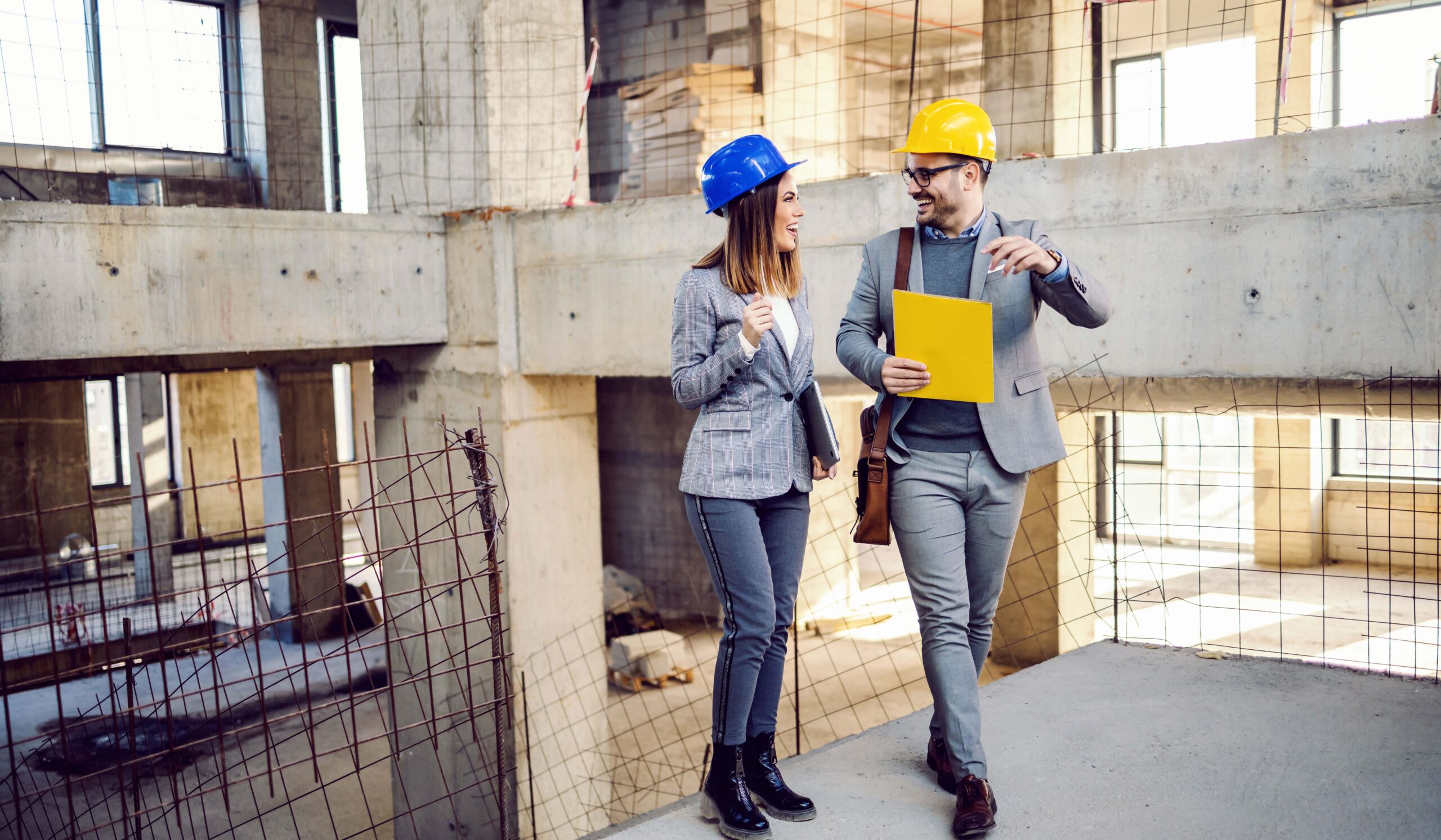 Two successful architects with helmets on heads walking in building in building process and talking about project thy created.